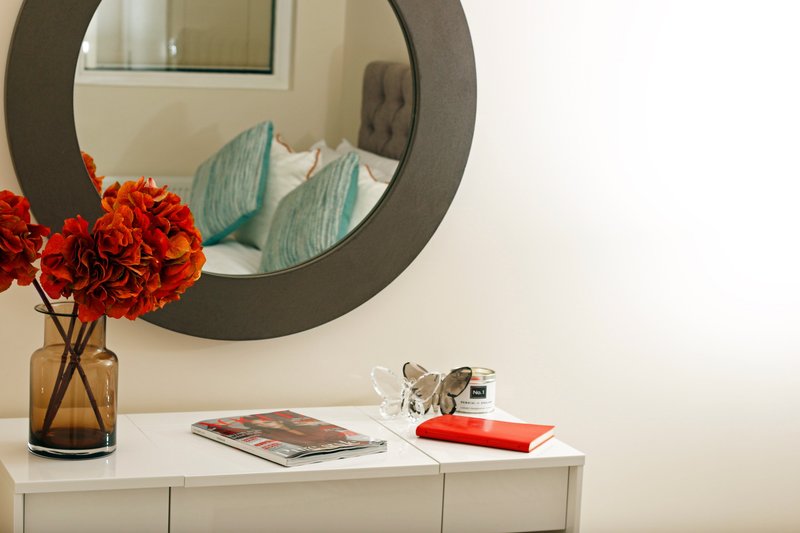 Bedroom dresser with round mirror, red flowers in vase, magazines and decor items