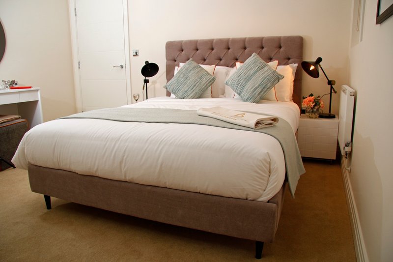Bedroom with brown upholstered bed, white bedding, decorative pillows, and bedside lamps
