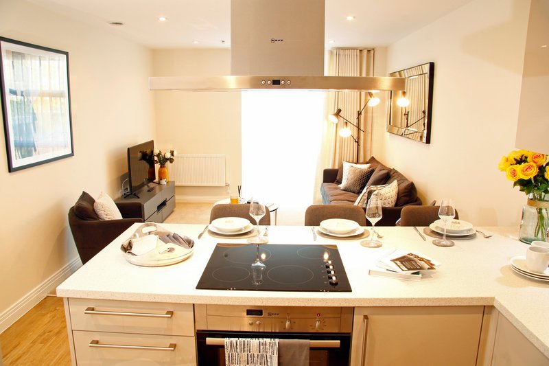 Modern kitchen with white island, cooktop, dining area and living room beyond