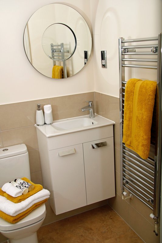 Modern bathroom with white vanity sink, round mirror, heated towel rail and yellow towels