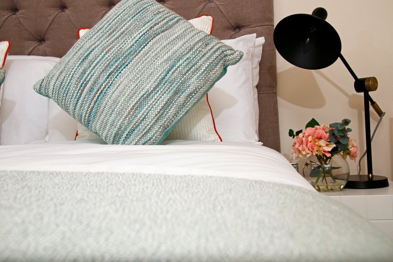 Bedroom with made bed, striped cushion, bedside lamp and fresh flowers in vase
