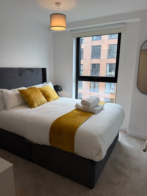 Modern bedroom with double bed, yellow cushions, pendant light and city view window
