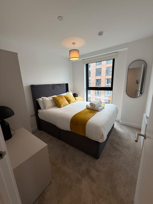Modern bedroom with double bed, yellow accents, pendant light and window view