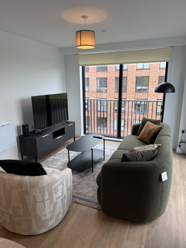 Modern living room with grey sofa, armchair, TV unit and balcony with brick building view