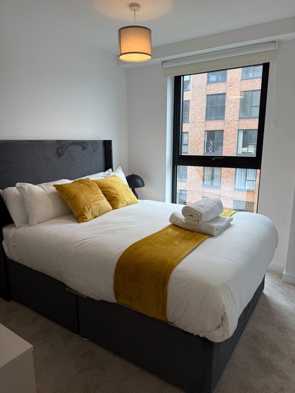 Modern bedroom with double bed, yellow cushions, pendant light and window view