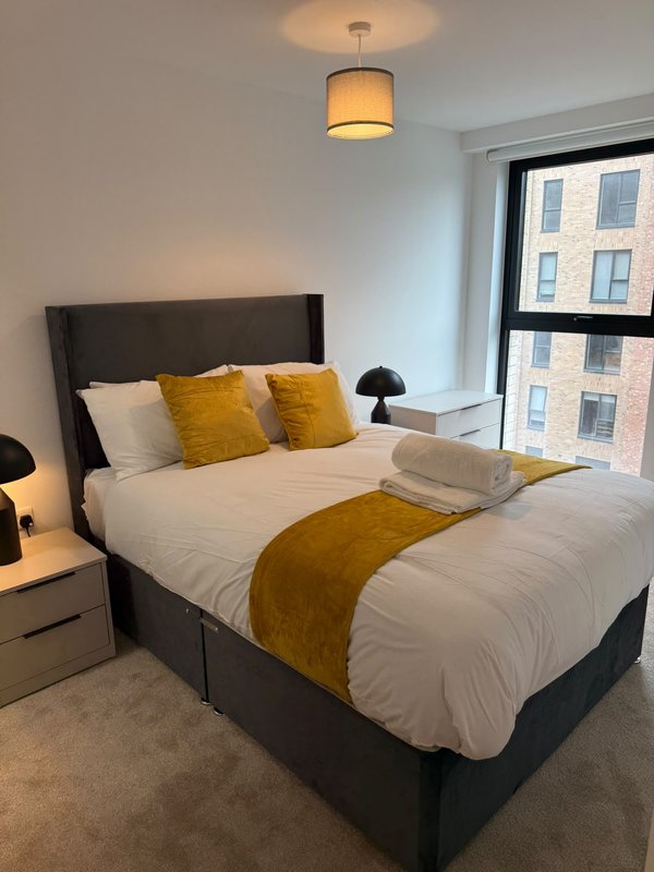 Modern bedroom with double bed, yellow cushions, bedside lamps and city views