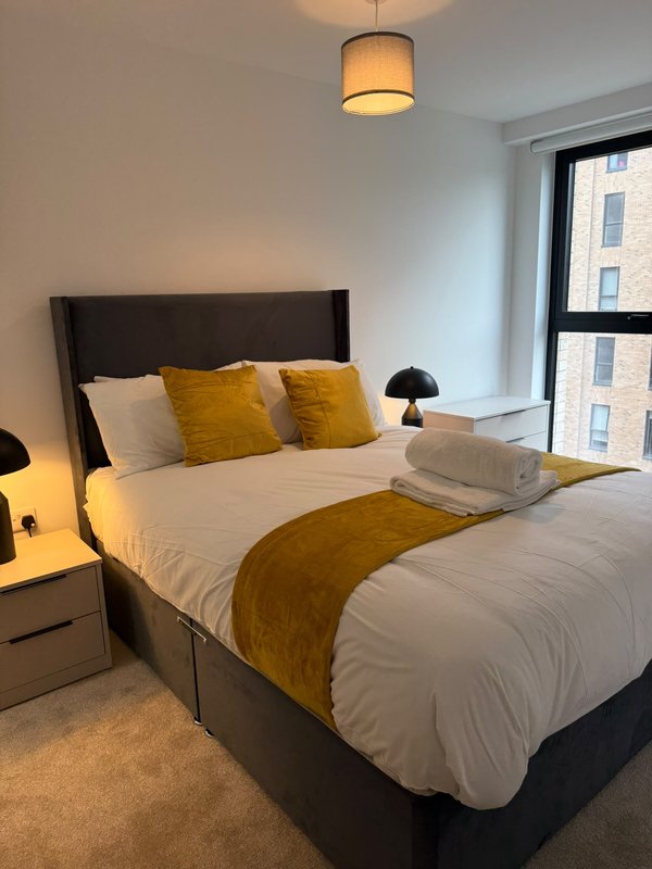 Modern bedroom with double bed, gold cushions, white bedding, pendant light and city view