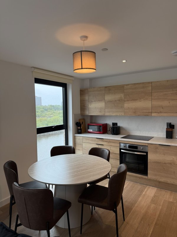 Modern kitchen with dining table, wooden cabinetry, built-in oven and pendant lighting