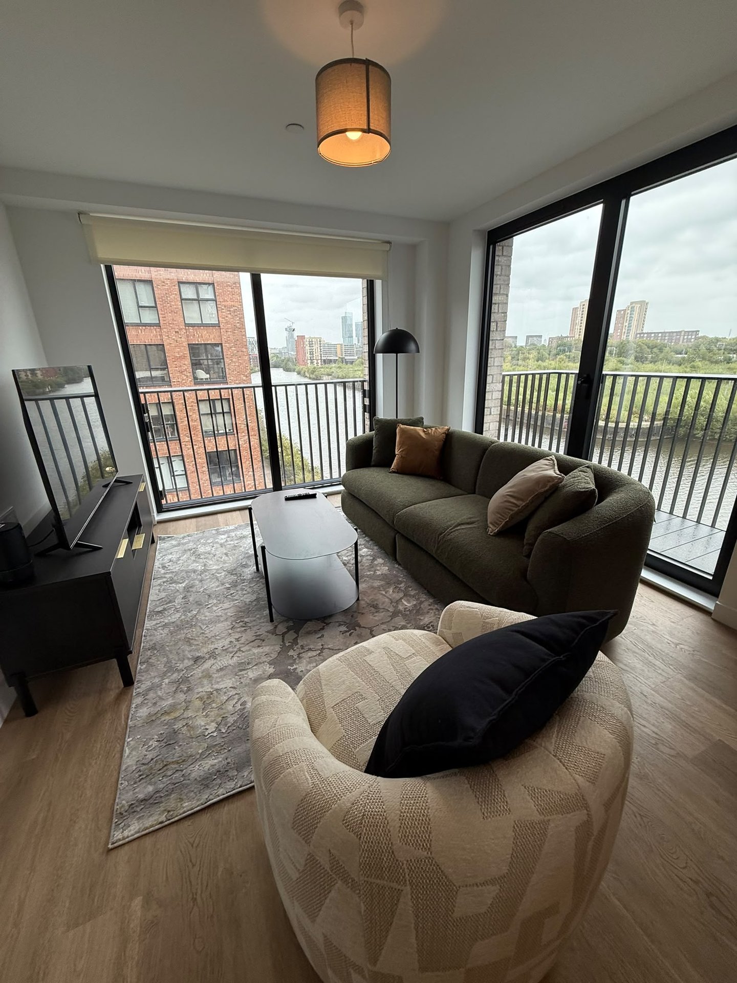 Modern apartment living room with sofa, armchair, wooden floor and city views from balcony