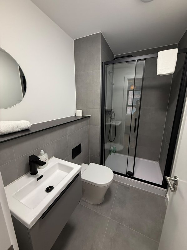 Modern bathroom with grey tile, white sink, toilet, and enclosed shower cubicle