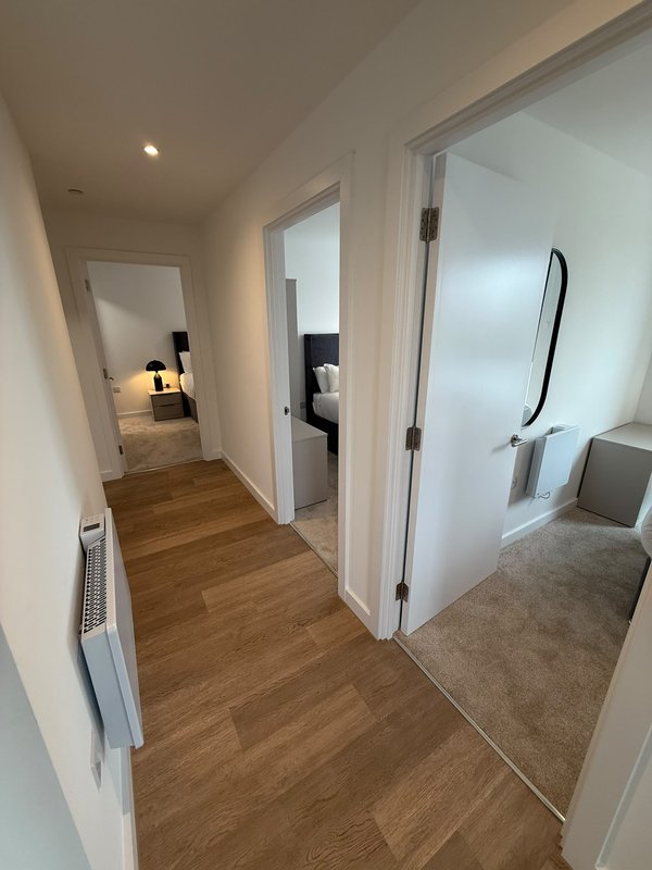 Modern hallway with wooden flooring, white doors, and access to multiple rooms