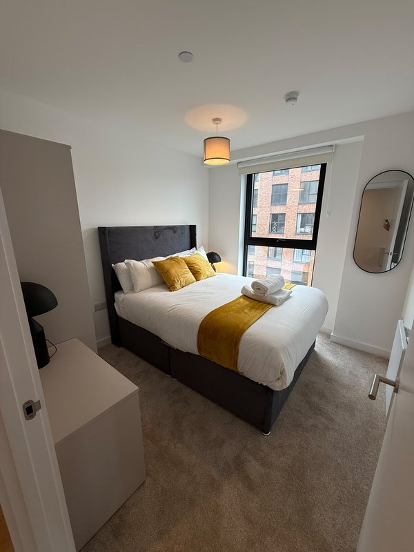 Modern bedroom with double bed, yellow throw, window with city view, pendant light