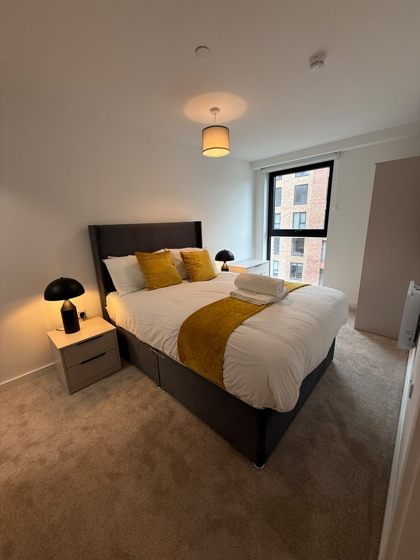 Modern bedroom with double bed, gold throw, black headboard, bedside lamp and window