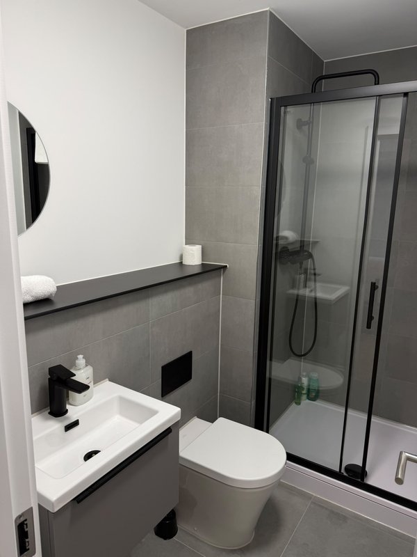 Modern bathroom with white toilet, gray tile walls, sink and black-framed shower enclosure