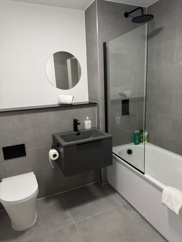 Modern bathroom with toilet, floating vanity, round mirror, shower enclosure and grey tile walls