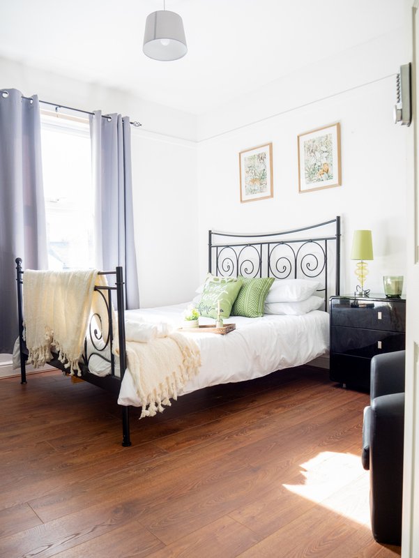 Bright bedroom with black metal bed frame, white bedding, wooden floor and purple curtains