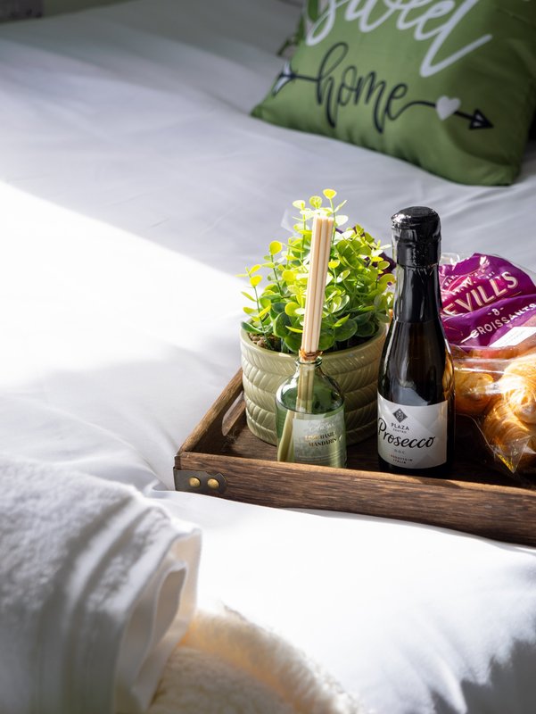 Bed tray with potted flowers, prosecco bottle, and decorative items on white bedding