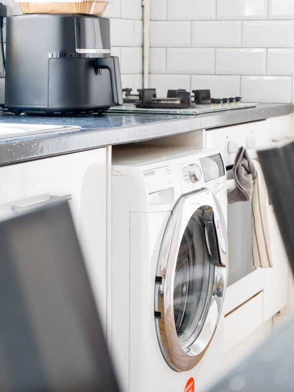 Kitchen with washing machine, countertop, kettle and white subway tile backsplash