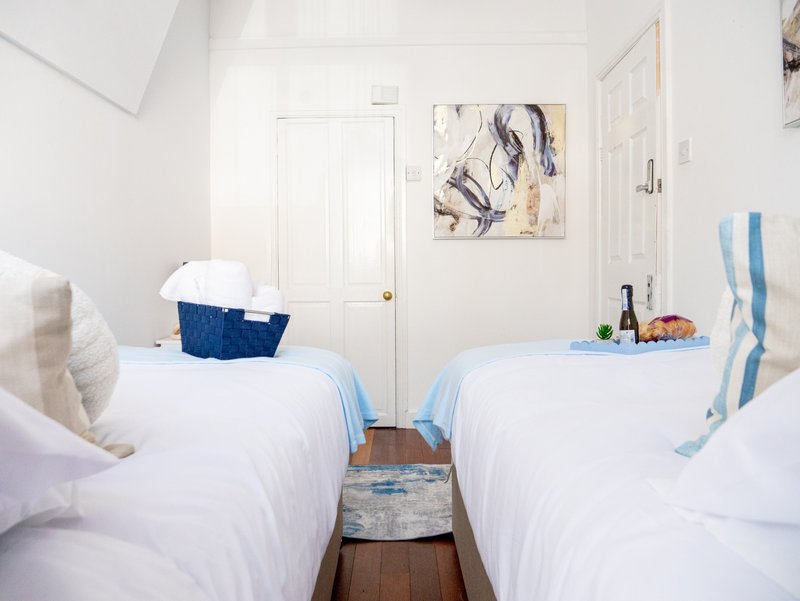Bright twin bedroom with two white beds, blue accents, wooden floor and wall art