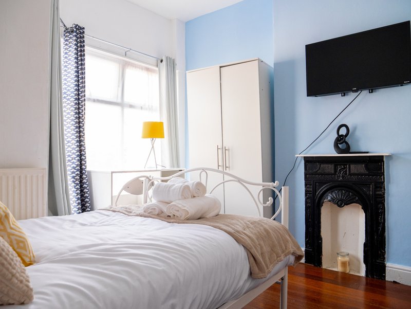 Bright bedroom with metal bed frame, white bedding, blue accent wall and mounted TV