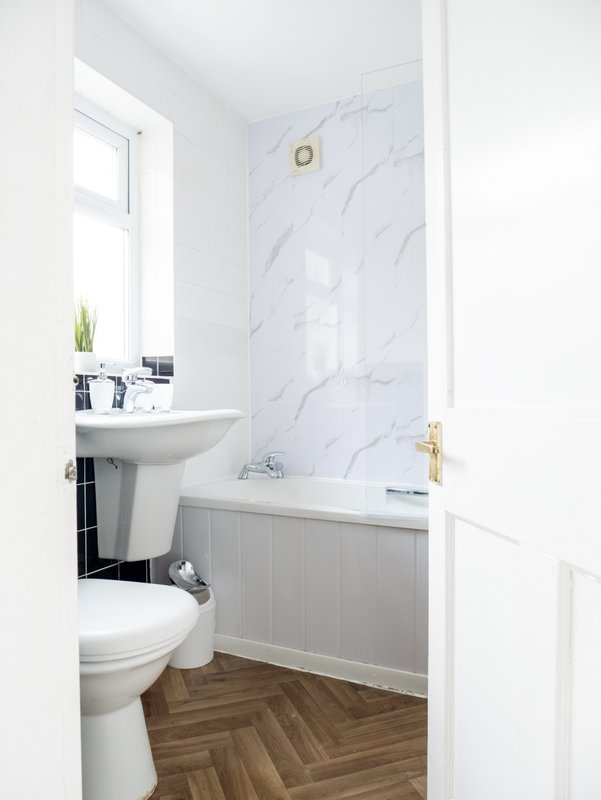 Modern bathroom with white sink, toilet, bathtub, marble wall tile and wooden floor
