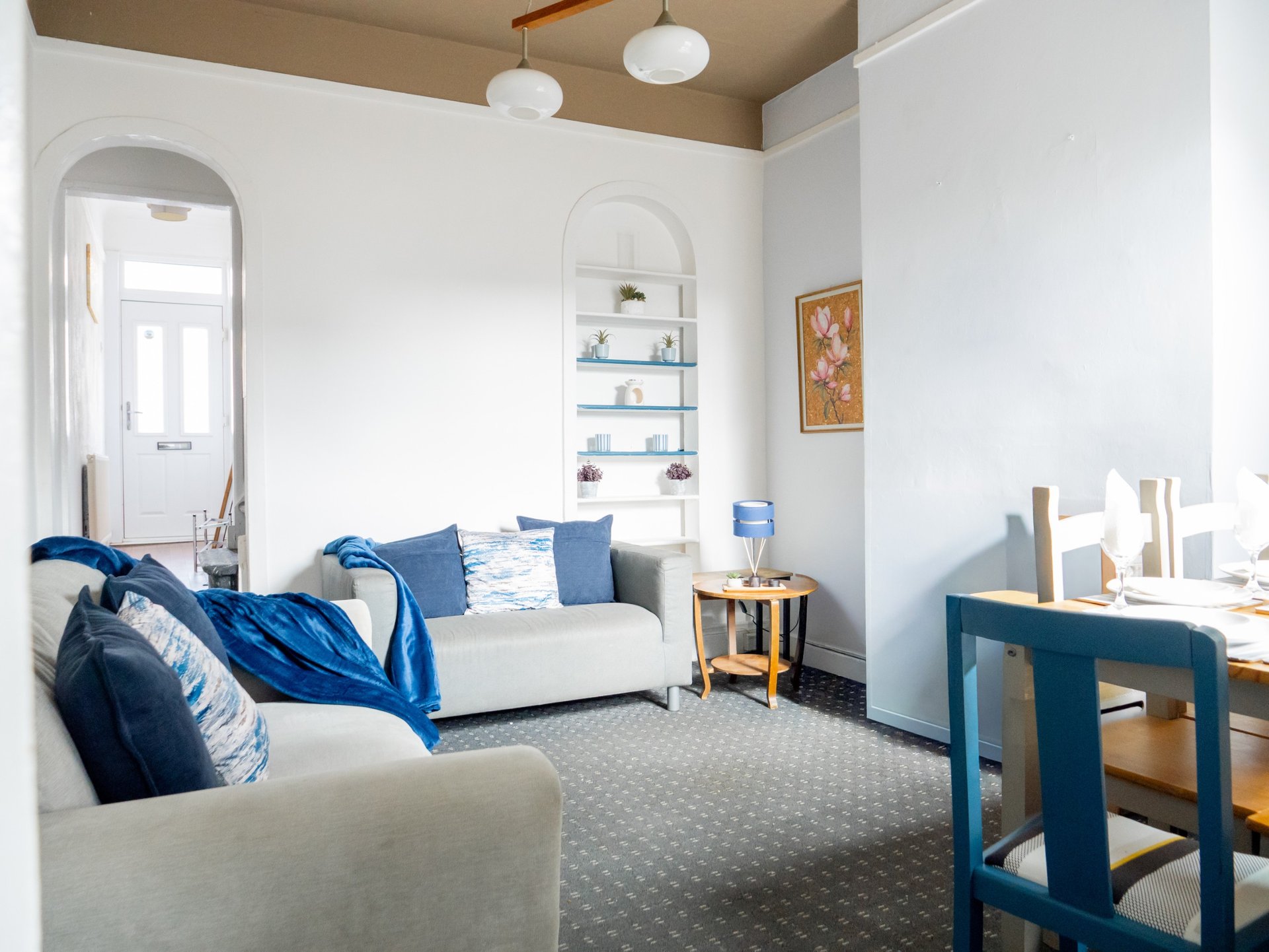 Bright living room with white sofa, blue cushions, mirror, shelving, desk and wooden furniture