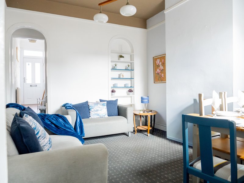 Bright living room with white sofa, blue cushions, mirror, shelving, desk and wooden furniture