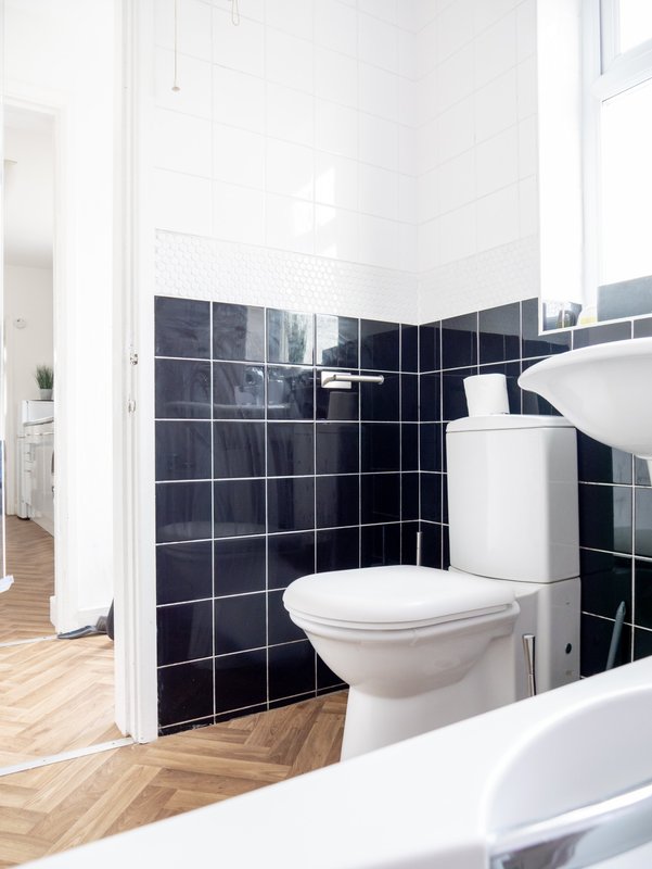 Modern bathroom with black tile walls, white toilet, sink, and herringbone wood flooring