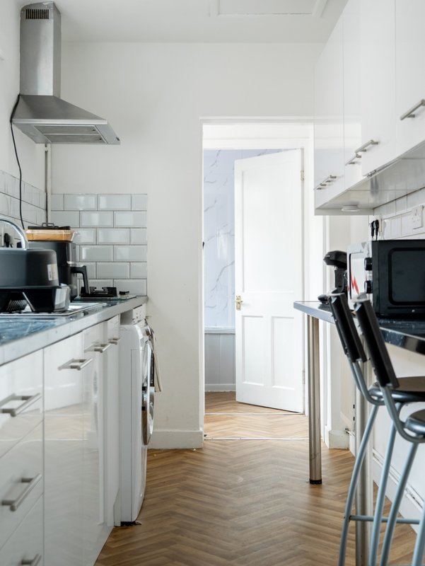 Modern kitchen with white cabinetry, stainless steel range hood, subway tile backsplash and wooden flooring