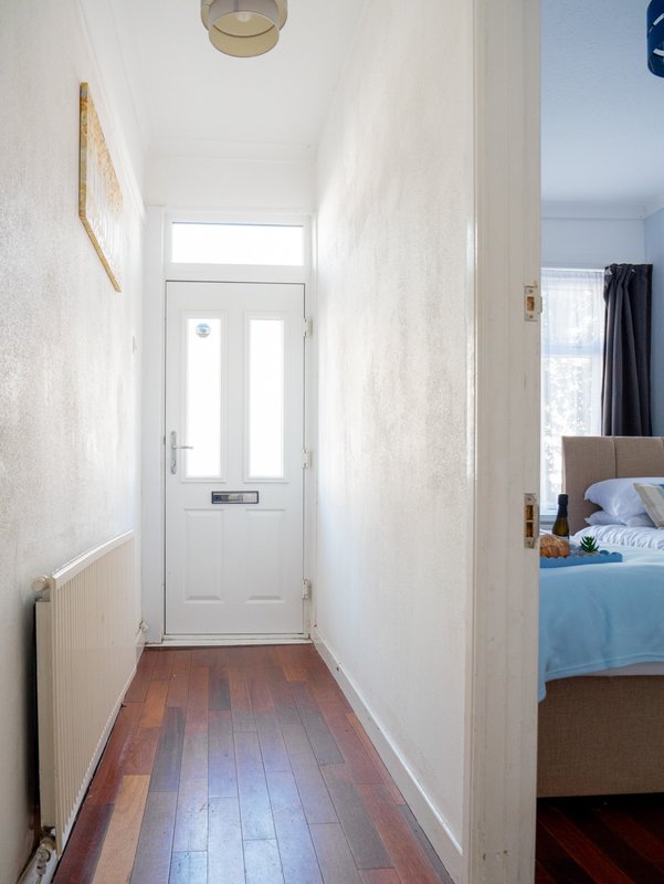 Narrow hallway with white walls, wooden floor, and white entrance door with window panes