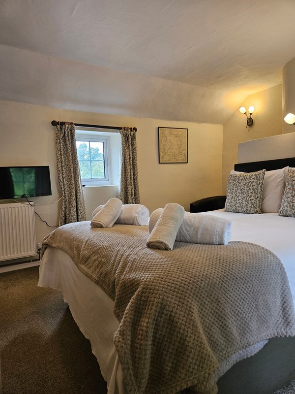 Bedroom with double bed, patterned bedding, window with curtains, wall-mounted TV, and wall sconce lighting