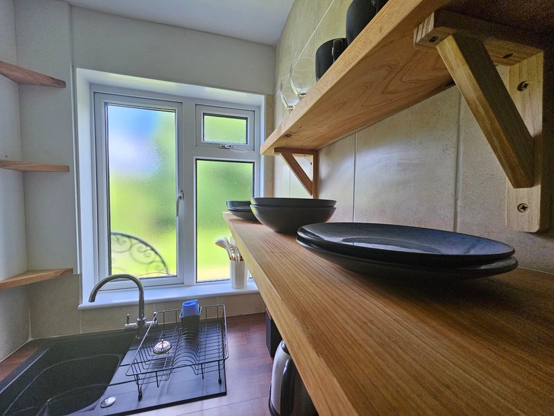Modern kitchen with wooden countertops, black sink bowls, stainless steel tap, and garden views through double doors