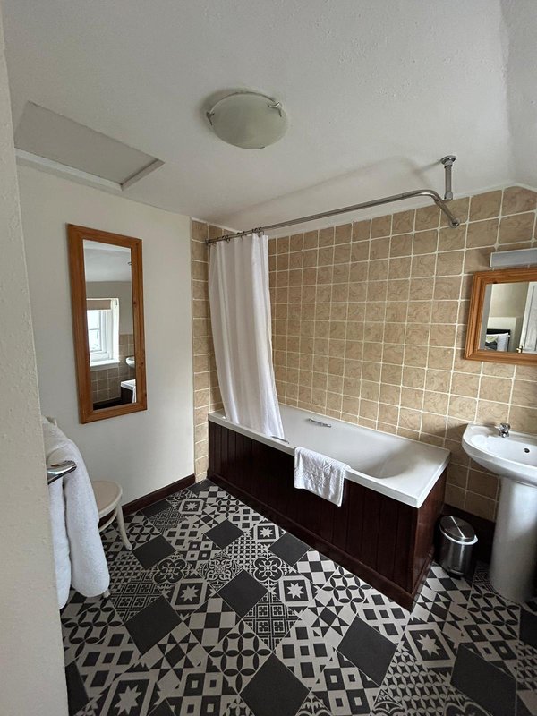 Bathroom with bathtub, sink, mirrors, tiled walls and patterned floor
