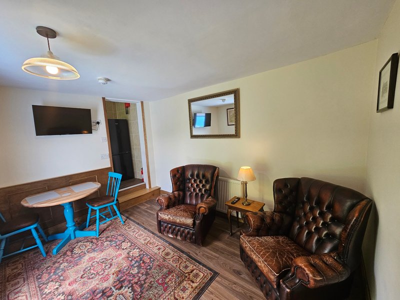 Living room with leather armchairs, wooden table, blue stool, wall-mounted TV and warm lighting