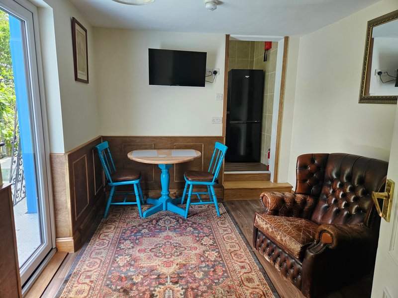 Living room with blue chairs, round table, brown leather armchair, TV, and patterned rug