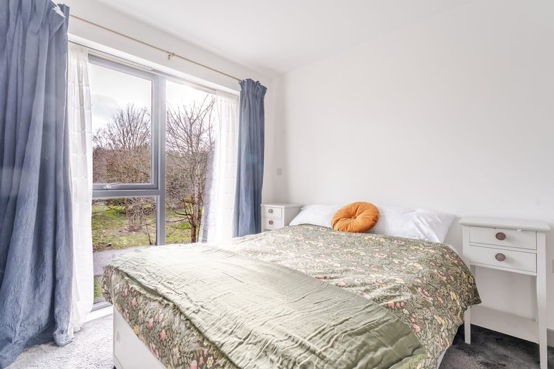 Bright bedroom with double bed, white bedside table, blue curtains and garden view