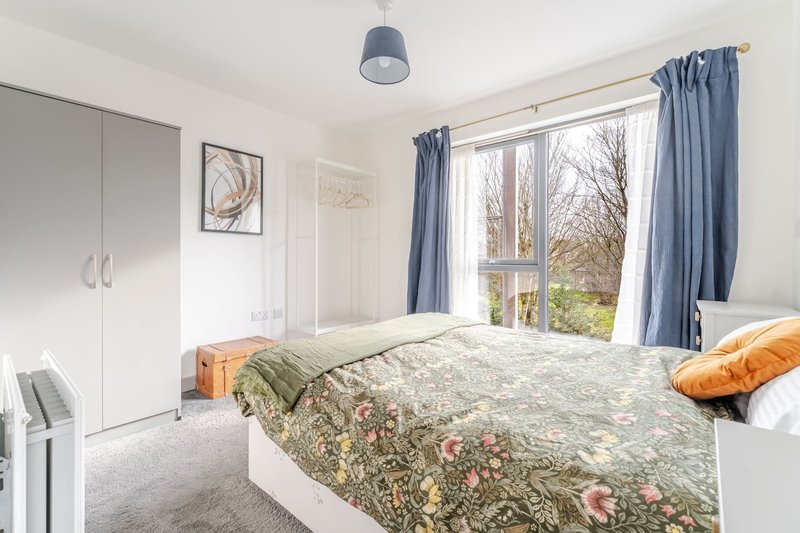 Bright bedroom with double bed, blue curtains, white wardrobe and pendant light