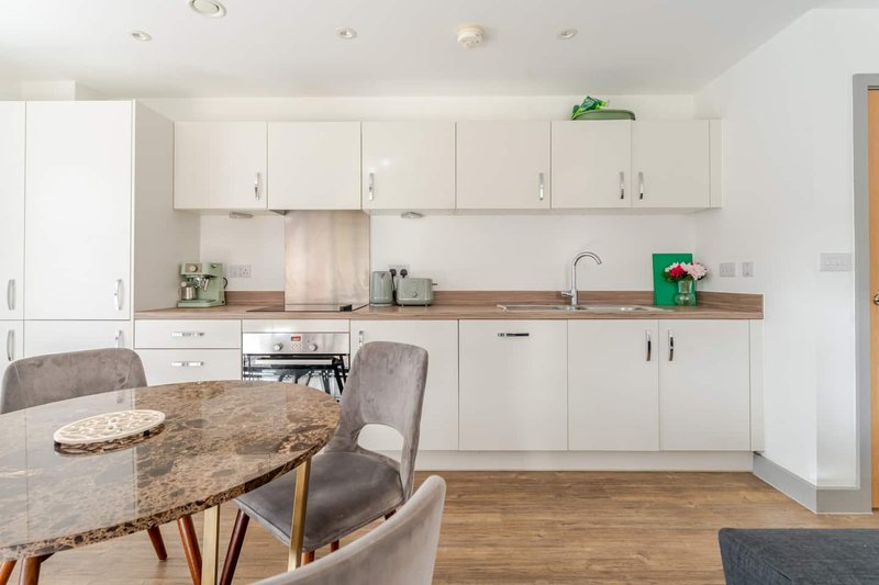 Modern kitchen with white cabinetry, wooden countertops, dining table and grey upholstered chairs