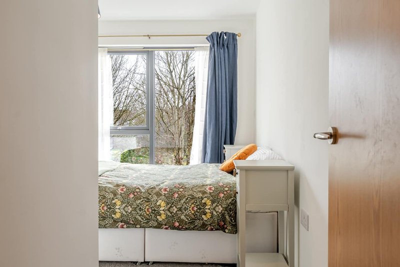Bright bedroom with single bed, blue curtains, window view and wooden door