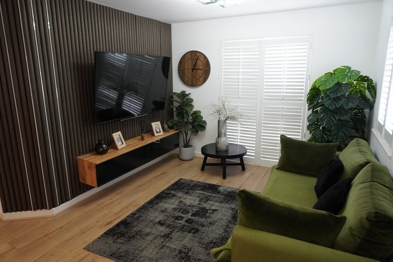 Modern living room with green sofa, TV on wooden stand, wooden flooring and large plant