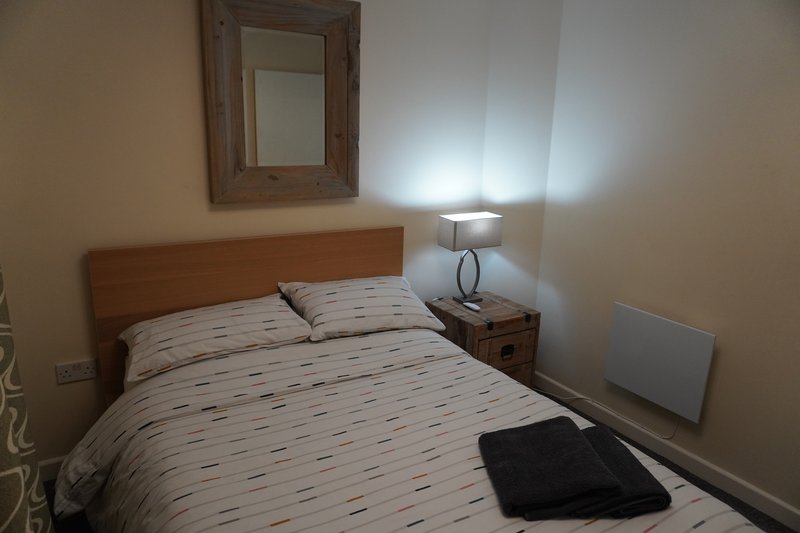 Bedroom with double bed, wooden headboard, bedside lamp and mirror on wall