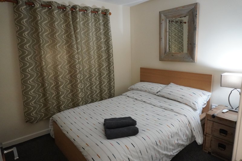 Bedroom with double bed, wooden headboard, patterned curtains and bedside table