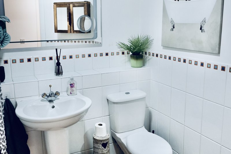 Clean bathroom with pedestal sink, toilet, white tile walls, and decorative mirror