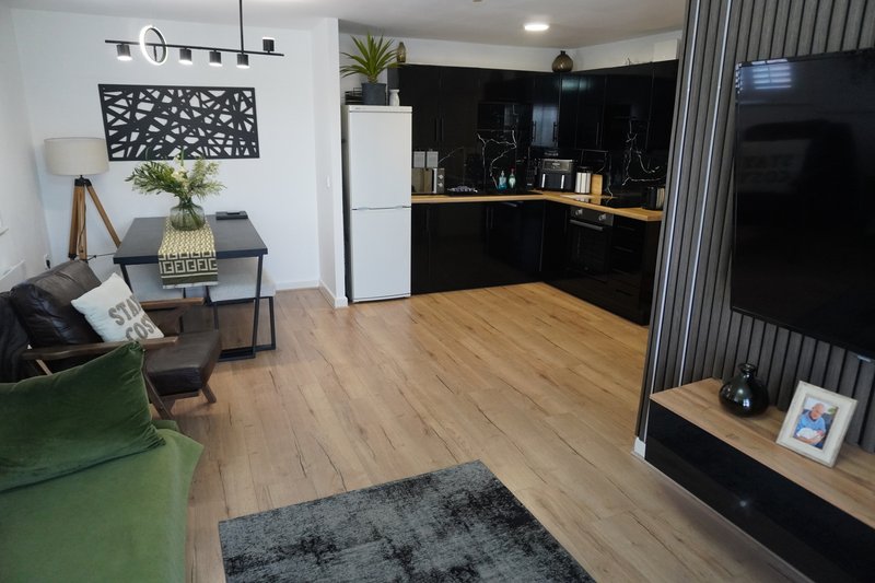 Open-plan living space with green sofa, wooden flooring, black kitchen, and TV entertainment area