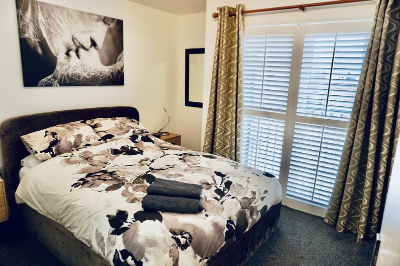 Bedroom with double bed, patterned bedding, wall art, shuttered doors and curtains