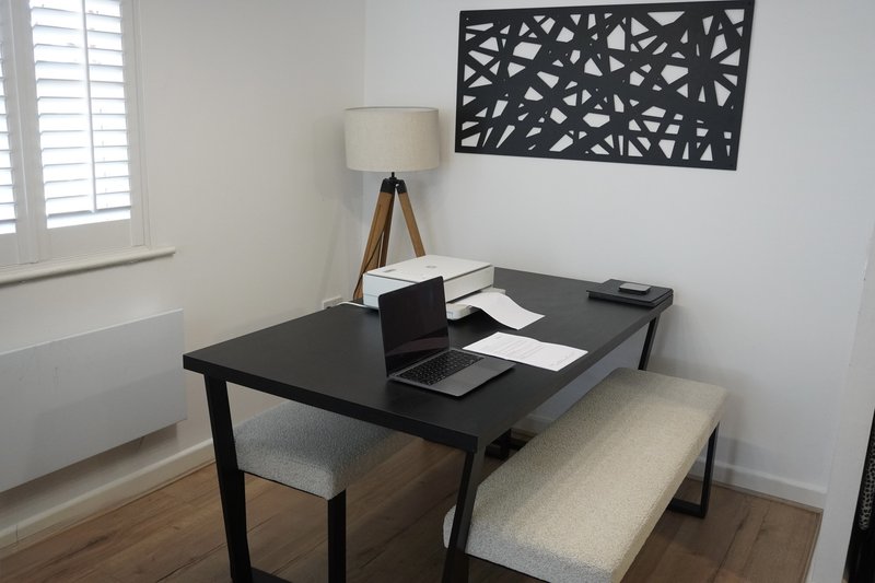 Modern home office with black desk, laptop, lamp, and decorative wall art
