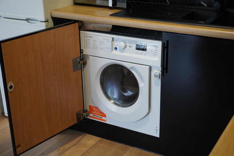 Built-in washing machine in kitchen unit with wooden cabinet door open