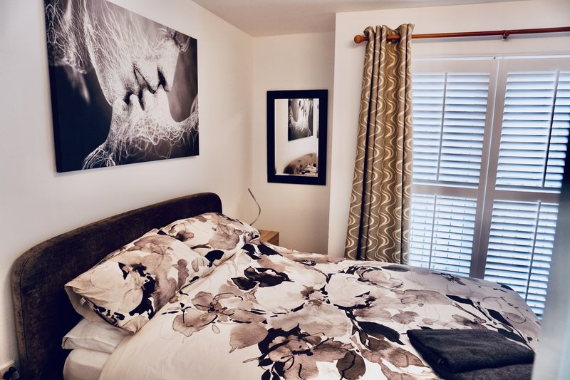Modern bedroom with double bed, patterned bedding, wall art, and shuttered doors