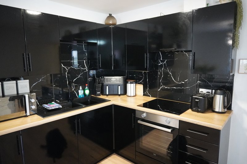 Modern kitchen with black cabinetry, wooden countertops, stainless steel appliances and pendant lighting