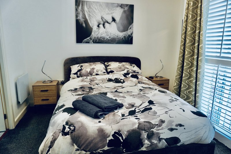 Bedroom with double bed, black headboard, patterned bedding, wooden nightstands and window with shutters